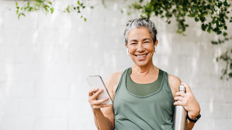 Motivated senior woman looking at the camera with a happy smile as she browses her smartphone for some music outdoors. This elderly woman is taking on an active lifestyle, maintaining her physical wellness through regular exercise.